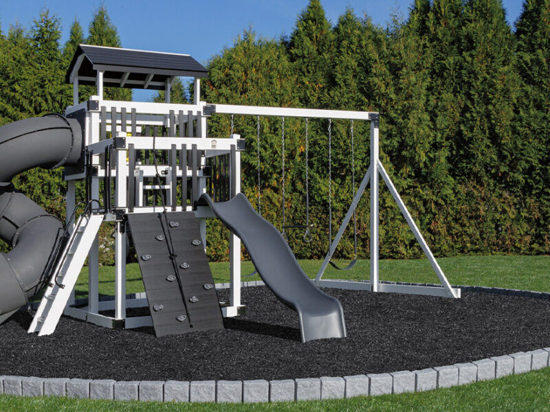 White and gray vinyl Discovery Depot swing set with a green spiral slide, wave slide, and three-position swing beam on a grass lawn.