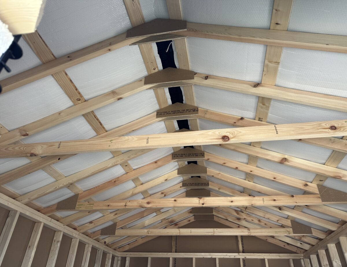 Interior roof framing of a 12x16 storage shed with double bubble radiant barrier insulation and sturdy wooden rafters.