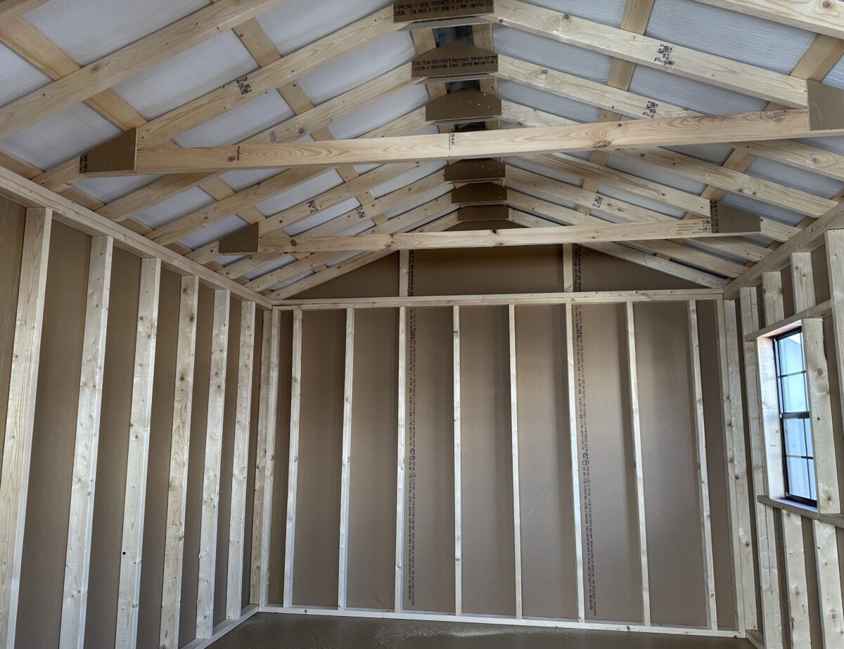 Interior corner view of a 12x16 storage shed with wooden wall studs, top plate framing, and high-performance flooring.