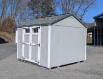 10×10 Madison Peak shed with light gray LP SmartSide siding, white trim, and shadow gray shingles, featuring double barn doors with transom windows and black hardware, displayed on a gravel lot.