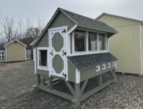 A 6x8 wooden chicken coop with green LP siding, white trim, and a grey shingled roof, featuring a human-sized entry door and windows.
