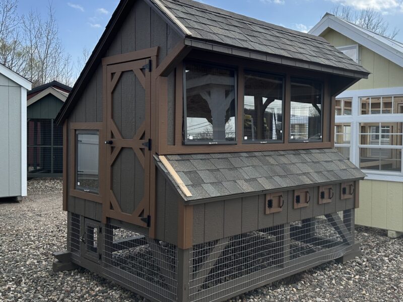 A 6x8 wooden chicken coop with green LP siding, white trim, and a grey shingled roof, featuring a human-sized entry door and windows.