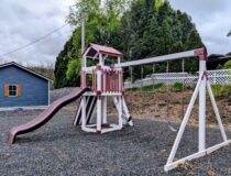 Vinyl swing set with slide, tower, belt swings, and trapeze rings in backyard setting