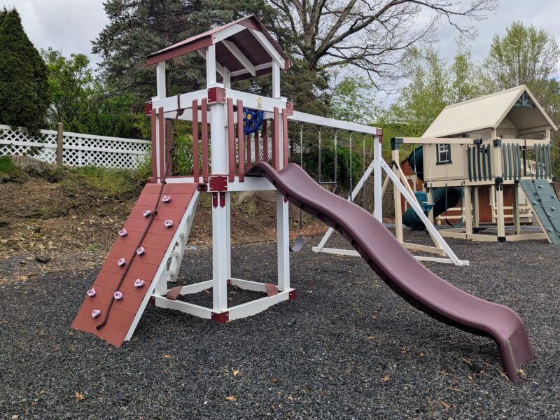 Vinyl playset with tower, climbing wall, rope, and curved slide on mulch ground