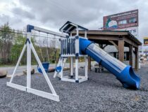Vinyl-sleeved pressure treated wood playset with tube slide, clubhouse, and bucket swings on gravel lot