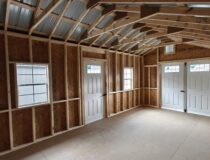Interior framing of a 12x20 Cottage Shed showing wood studs, OSB walls, and natural light from transom windows.