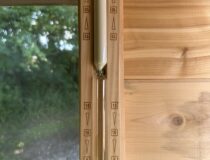 A 15-minute wooden hourglass sand timer mounted on the interior white cedar wall of an outdoor sauna.