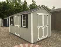 8x14 Light Grey Madison Peak shed with white trim, black shutters, and double doors on a gravel pad.