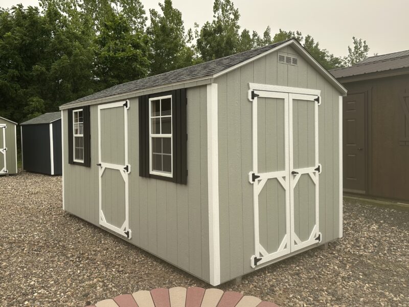 8x14 Light Grey Madison Peak shed with white trim, black shutters, and double doors on a gravel pad.
