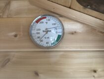 Analog sauna thermometer and hygrometer gauge displaying temperature and relative humidity inside an 8x12 sauna.