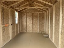 Wood-framed interior of an 8x14 Madison Peak shed showing the floor, wall studs, and roof trusses.