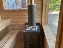 Interior shot of an outdoor sauna stove with rocks alongside white cedar benches and fresh oxygen intake vents.